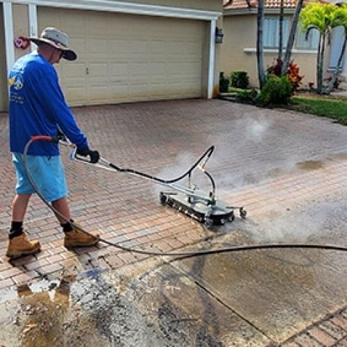 Technician pressure washing a residential driveway to remove dirt and stains, improving curb appeal for a Florida Keys home.